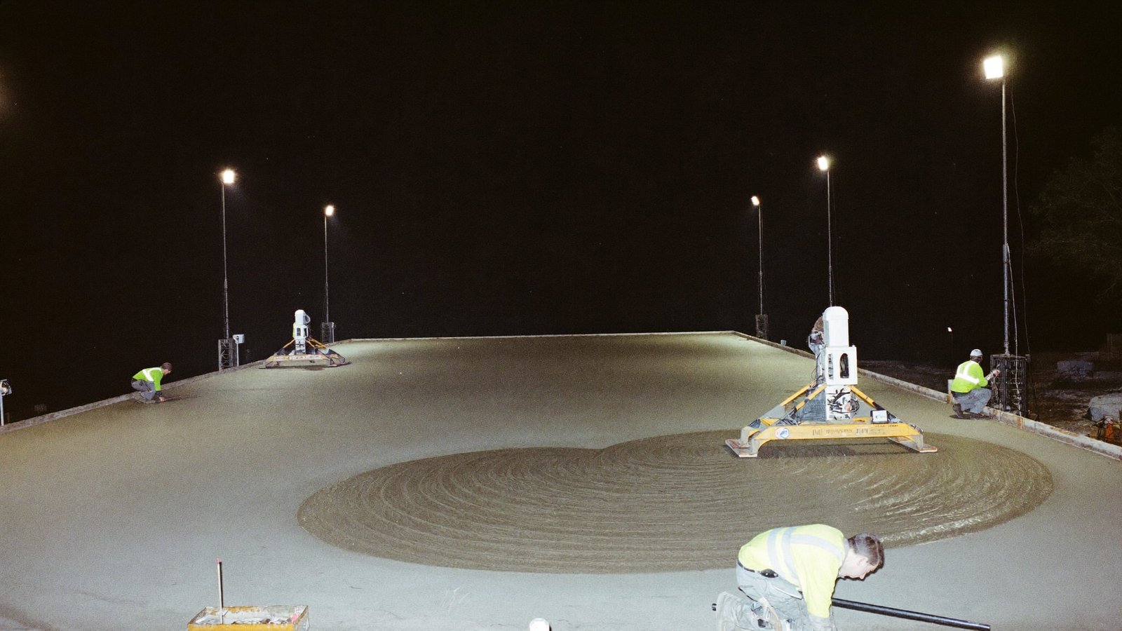 Concrete crew finishing a slab pour under lights at night
